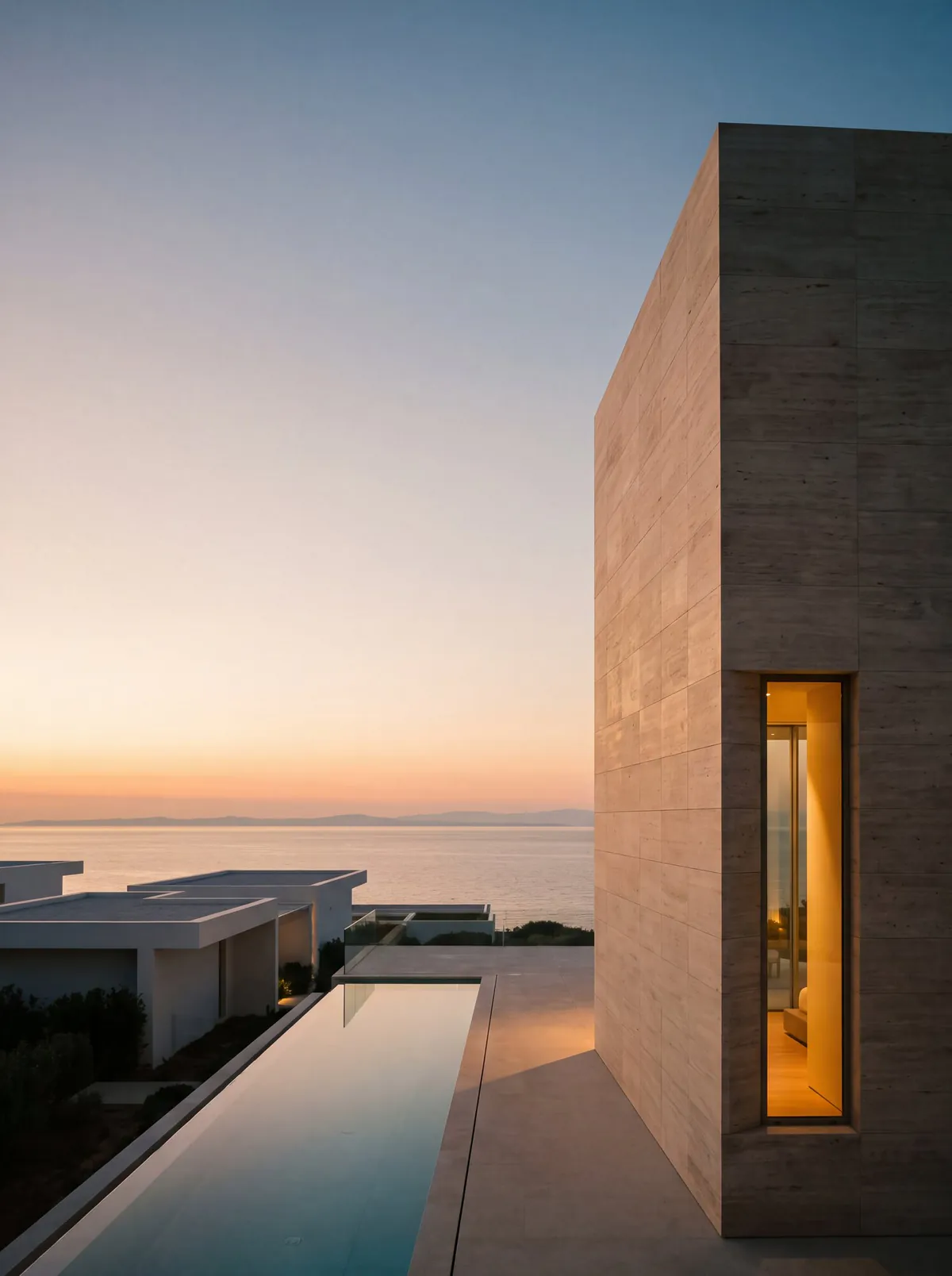 Travertine villa above the sea at sunset, with a long pool between the houses